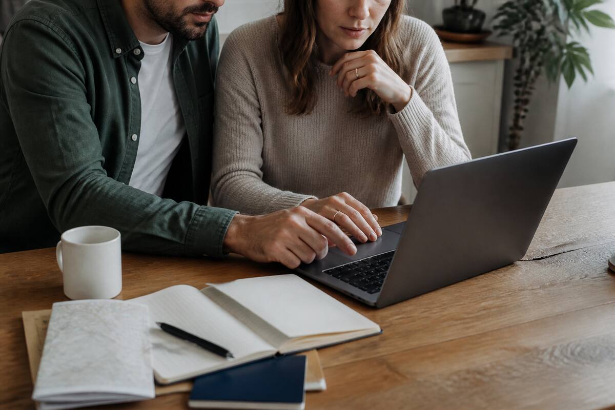 Een stel vergelijkt vakantieopties op een laptop aan een keukentafel met reisnotities